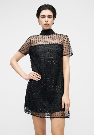 Short black dress with a sheer, textured overlay featuring a grid pattern and a high neckline. Short sleeves and a relaxed cut.