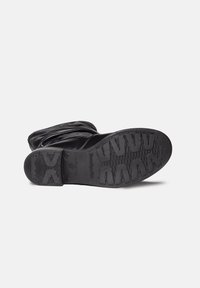 Musta nahkasaapas nilkkapituudella, jossa on teksturoitu pohja, jossa on sahalaitakuviota ja logosomistus. Yläosa on löysä, mikä lisää rakennetta.