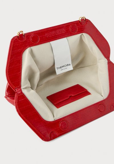 Κόκκινη δερμάτινη τσάντα χειρός ανοιχτή, που αποκαλύπτει το εσωτερικό από κρεμ ύφασμα και ένα κόκκινο δερμάτινο θήκη καρτών με μια λευκή ετικέτα που αναγράφει «THEMOIRè Made in Italy».