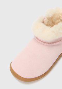 Botte en daim rose clair avec une doublure en fourrure crème douce et une semelle en caoutchouc, présentant un bout rond et des détails cousus sur le dessus.