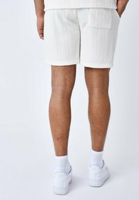 I pantaloni corti bianchi in tessuto testurizzato presentano righe verticali e una tasca sul retro. Abbinati a sneaker bianche e calze, si focalizzano su un'estetica pulita e neutra.