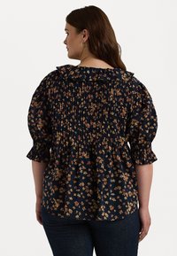 Mørkeblå blomsterbluse med smocking, volangkrave og puffede ærmer. Har små gule og orange blomster mod en mørk baggrund.