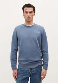 Lichtblauwe sweatshirt van zacht materiaal, met een ronde halslijn, lange mouwen en een klein wit logo op de borst.