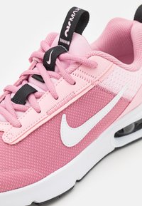 Scarpa sportiva rosa con tomaia in tessuto a rete testurizzato, logo swoosh bianco, lacci neri e collare imbottito. Suola bianca con ammortizzazione ad aria visibile.