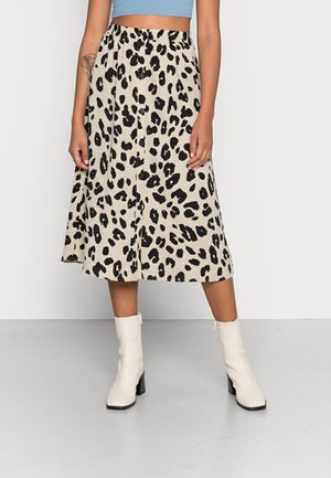 Femme portant une jupe midi beige à imprimé léopard noir avec des boutons à l'avant, associée à des bottines blanches et un top court bleu.