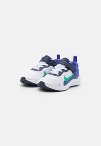 Baltas sporta apavu pāris ar tumši zilām akcentiem, zaļu S swoosh, purpursarkanu papēdi un lentu ar uzlīmi. Iezīmē teksturētu augšpusi un gumijas zoli.