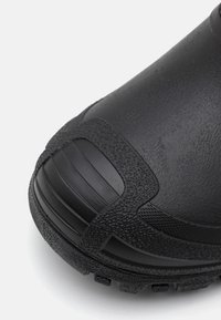 Botas de goma negras con superficie texturizada, punta reforzada y suela texturizada. Elementos suaves y rugosos mejoran la tracción y la durabilidad.