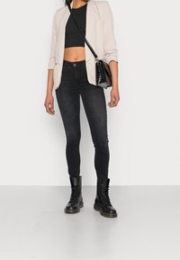 Czarne wąskie dżinsy, skrócona czarna bluzka, jasnobeżowa marynarka i czarne lace-up botki. Czarna torba o teksturowanym wykończeniu z paskiem na ramię.