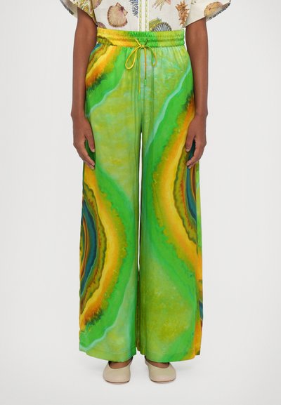 Weite Hosen in Grün mit einem welligen gelben und blauen Muster. Hergestellt aus weichem Stoff, mit einem elastischen Bund und einem Zugband.