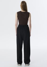 Top sin mangas marrón y pantalones holgados negros. El top presenta una textura acanalada; los pantalones tienen una cinturilla elástica y un bolsillo lateral.