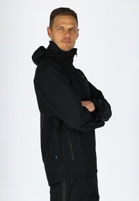Black waterproof jacket with a high collar, zippered front, and elastic cuffs. Features a subtle logo and side pockets for functionality.