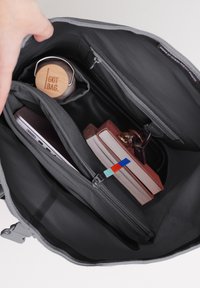 Intérieur d'un sac en tissu gris avec des compartiments. Contient une bouteille d'eau en bois, un ordinateur portable, des cahiers et un porte-clés, avec des détails de fermeture éclair colorés.