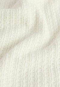 Měkká bílá pletená látka s žebrovanou strukturou a jemnými diagonálními záhyby vytvářejícími jemné stíny.