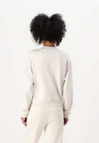 Sudadera de color gris claro, fabricada en suave algodón, con mangas largas, puños acanalados y un cuello alto con un corte relajado.