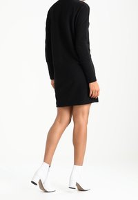 Robe noire à manches longues atteignant le mi-thigh, associée à des bottines blanches à talon bloqué et fermeture éclair.