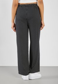 Black wide-leg pants with a white polka dot pattern, elastic waistband, and a smooth texture, paired with white sneakers.