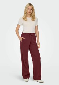Maron brede sweatpants med elastisk talje og snøre, der har sidelommer, parret med en hvid tætsiddende t-shirt.