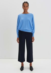 Maglione lavorato a maglia azzurro chiaro con maniche larghe, abbinato a pantaloni neri a gamba larga e scarpe slip-on nere. Design semplice, texture morbida.