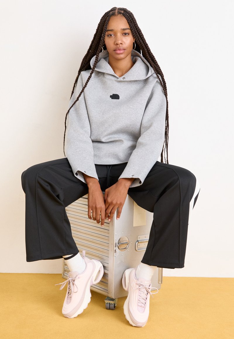 Sudadera gris de gran tamaño con un logo negro, combinada con pantalones anchos negros y zapatillas rosa claro. Fondo amarillo.