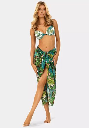 Bikini z białym tłem z zielonymi wzorami liści; przezroczysty, wielokolorowy sarong w odcieniach zieleni z zawiązanym w pasie i wysokim rozcięciem, podkreślający żywe wzory.