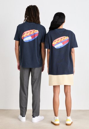 Camisetas de algodón azul marino con un gran gráfico de perrito caliente en la parte trasera. El diseño incluye acentos coloridos y formas redondeadas.