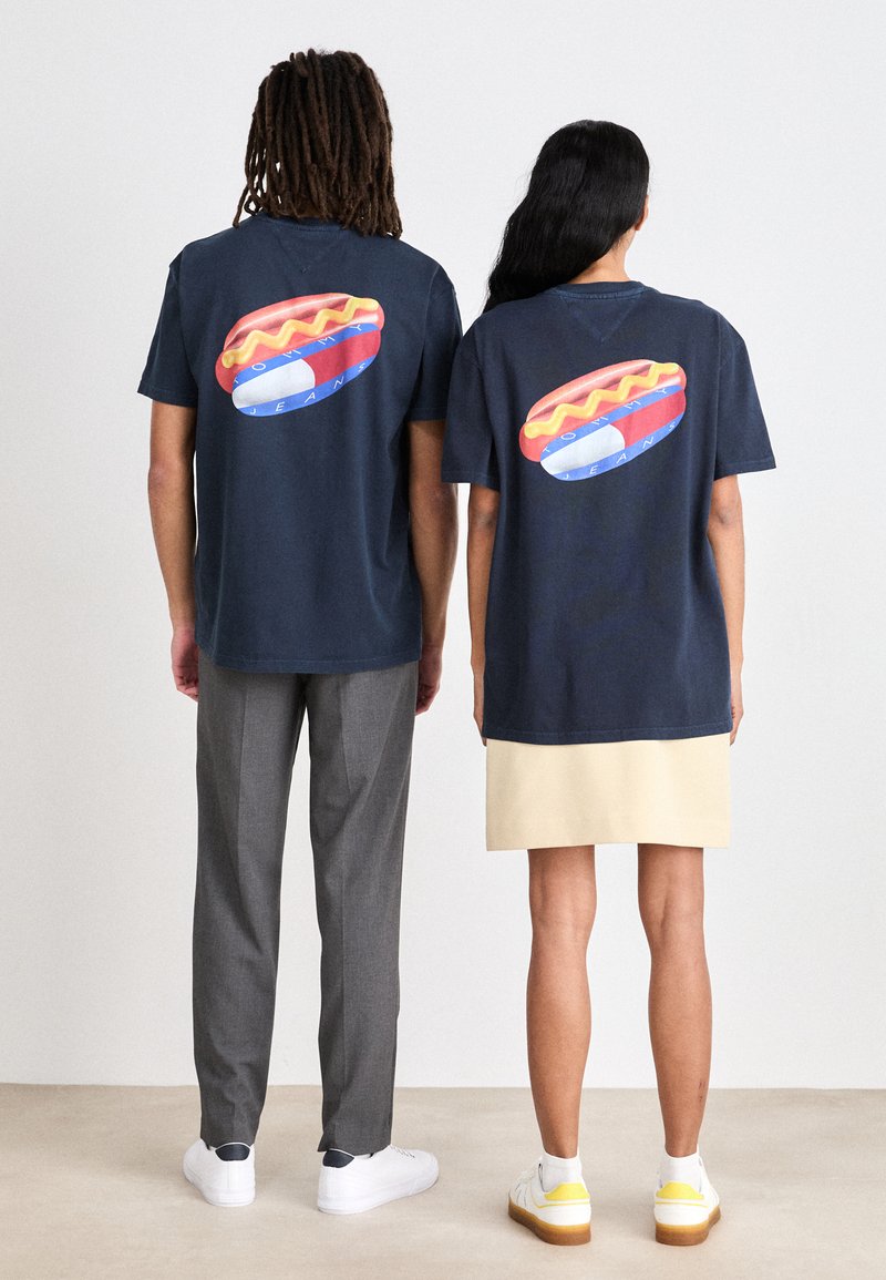 Camisetas de algodón azul marino con un gran gráfico de perrito caliente en la parte trasera. El diseño incluye acentos coloridos y formas redondeadas.