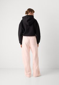 Haut à capuche noir coupé, associé à un pantalon de jogging rose clair à coupe décontractée avec une poche arrière. Tissu doux, design décontracté.