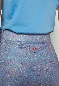 Modrý atletický top v kombinaci s přiléhavými legínami se světlomodrým pozadím a vícbarevným puntíkovým vzorem v červené a žluté barvě.