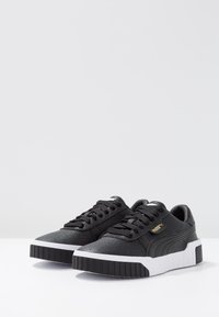 Czarne skórzane sneakersy z perforowaną strukturą, biała gumowa podeszwa, sznurowana konstrukcja oraz złoty akcent logo z boku.