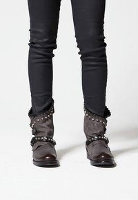 Gray boots with studded accents and ruffled tops, paired with tight black pants. Boots feature a shiny toe and textured fabric.