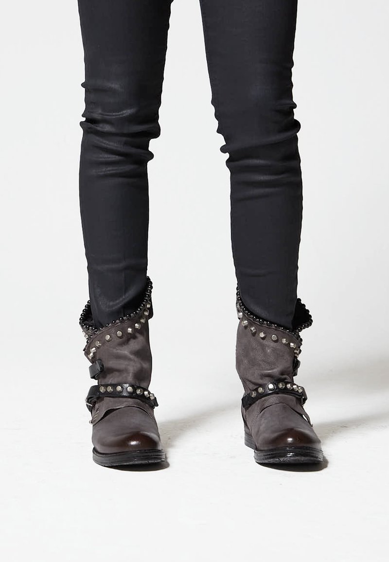 Gray boots with studded accents and ruffled tops, paired with tight black pants. Boots feature a shiny toe and textured fabric.