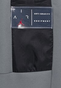 Svart och grått tygstycke med en sydd etikett som läser "AIR" och "ANTI-GRAVITY EQUIPMENT" bredvid en röd Jumpman-logotyp.