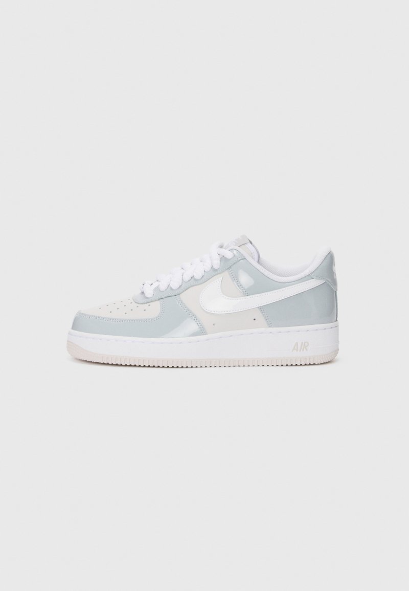 Nike Air Force 1 sneaker, világosszürke és fehér színben, sima bőrből és lakk részletekkel, lapos fehér fűzőkkel és gumitalppal.