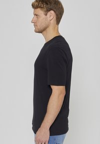 Μαύρο βαμβακερό t-shirt με κοντά μανίκια, λαιμόκοψη τύπου crew και άνετη εφαρμογή, φορεμένο με μπλε τζιν παντελόνι. Απλός και λιτός σχεδιασμός.