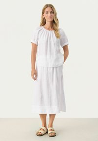 Weißes Leinenoberteil mit kurzen Ärmeln und gerafftem Ausschnitt, kombiniert mit einem weißen Leinenrock. Einfaches Design und leichtes Material.