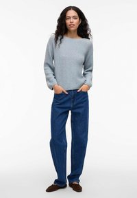 Jasnoniebieski sweter z plecionki z długimi rękawami, okrągłym dekoltem, zestawiony z ciemnoniebieskimi, luźnymi jeansami z wysokim stanem i brązowymi butami wsuwanymi.