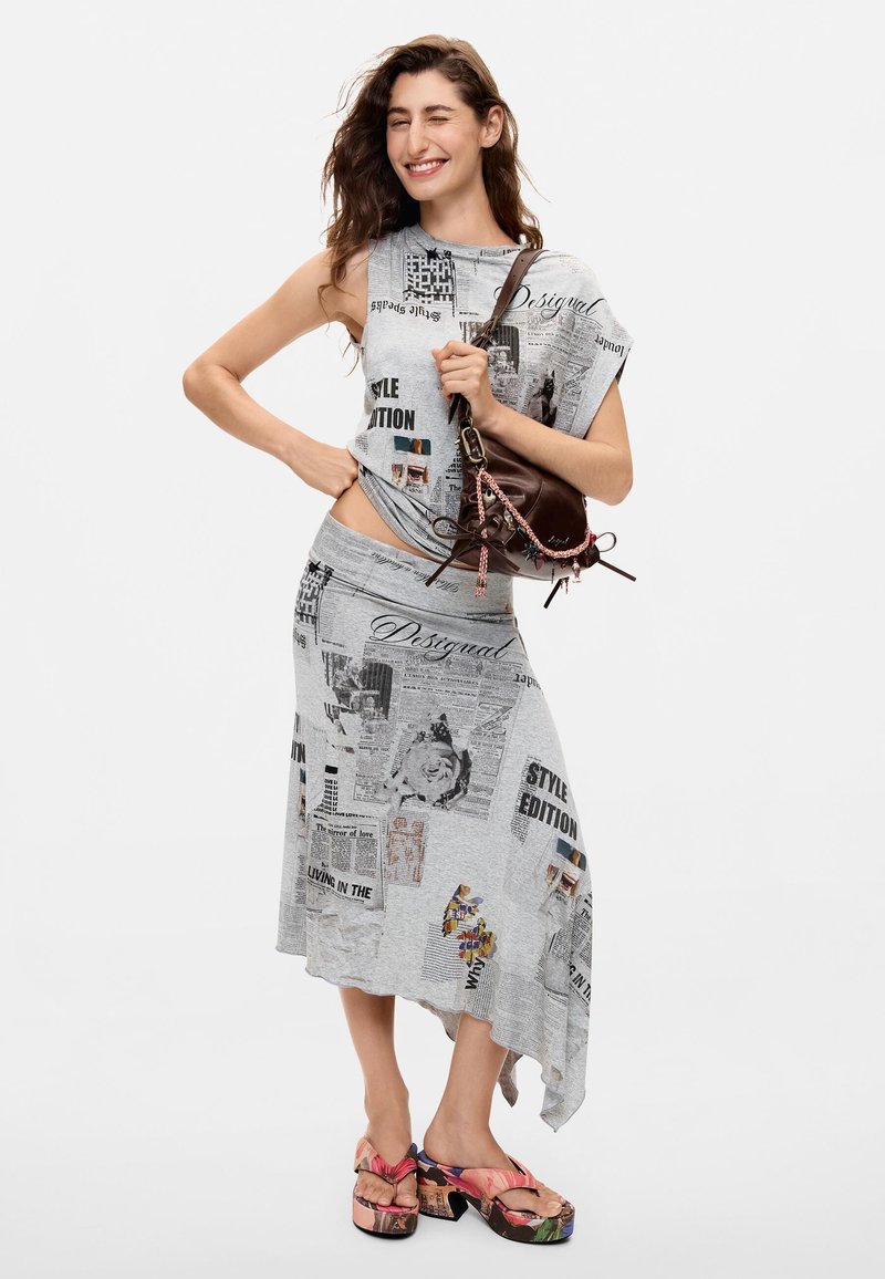 Woman wearing gray asymmetrical skirt and matching sleeveless top with newspaper print, pink platform sandals, and holding brown handbag.