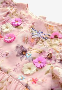 Blommönstrad rosa klänning i tyg med broderade blommor, paljetterad fjäril och texturerade detaljer. Volangärmar.