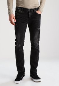 Svarta jeans i denim med blekningar, slitna detaljer och slim fit. I kombination med svarta sneakers. Långärmad tröja i neutrala toner.