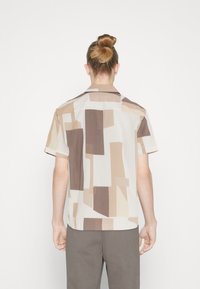 Camisa de manga corta en tejido liviano con un patrón abstracto geométrico en tonos beige y marrón. Cuello clásico con un ajuste relajado.