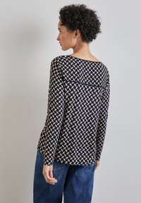 Laivastonsininen pitkähihainen paita, jossa on geometrinen vaalean kerma kuvio, veneen pääntie ja rento istuvuus. Yhdistetty sinisiin farkkuihin.