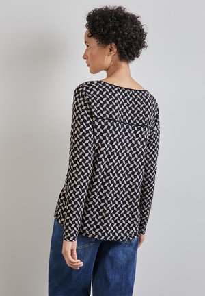 Mörkblå långärmad tröja med ett geometriskt mönster i krämfärg, med båthalsringning och avslappnad passform. I kombination med blå denimbyxor.