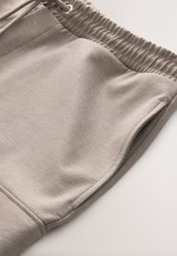 Pantaloncini sportivi beige con una texture morbida, vita elastica e tasche laterali. Il tessuto è liscio e appare leggero.