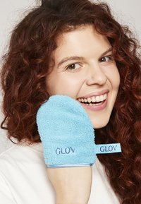 Turkusowa, teksturowana rękawica exfoliująca z logo "GLOV", prezentowana na dłoni, wykonana z miękkiego, puszystego materiału i o zaokrąglonym kształcie.