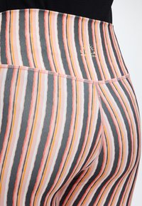 Κοντινό πλάνο ριγωτών κολάν με κάθετες ροζ, πορτοκαλί, λευκές και μαύρες γραμμές, που δείχνει τη μέση και τις λεπτομέρειες της ραφής.