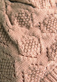 Tissu tricoté rose texturé avec des motifs géométriques en relief, arborant une finition douce et duveteuse. Le design comprend divers points.