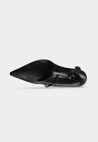Chaussure plate en cuir noir pointue vue de côté avec une bride basse et un petit talon noir sur fond blanc.