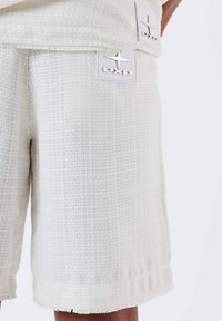 Shorts blancos texturizados con un patrón tejido, que presentan dobladillos deshilachados y dos parches del logo PXP en material contrastante.