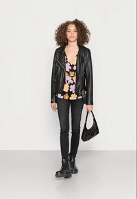 Jaqueta de couro preta, blusa com padrão floral em roxo, laranja e amarelo, jeans skinny pretos, botas de tornozelo pretas e uma pequena bolsa preta.