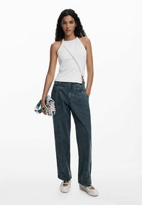 Valge kaelusega top, tumelised sinised lahtised püksid küljetaskutega ja heledates toonides libistatavad kingad. Model hoiab mustriga salli.